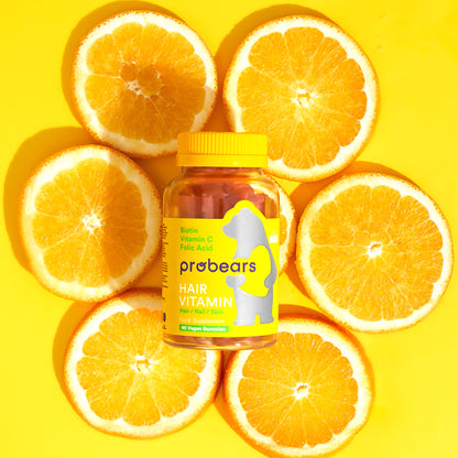Probears Haar-Vitamin Gummibärchen auf leuchtend gelbem Hintergrund mit Orangenscheiben, unterstreichen die natürlichen Inhaltsstoffe für Haargesundheit.